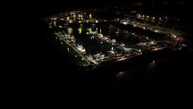 Aerial drone night shot of fishing harbour with lit wharves and fishing fleet docked